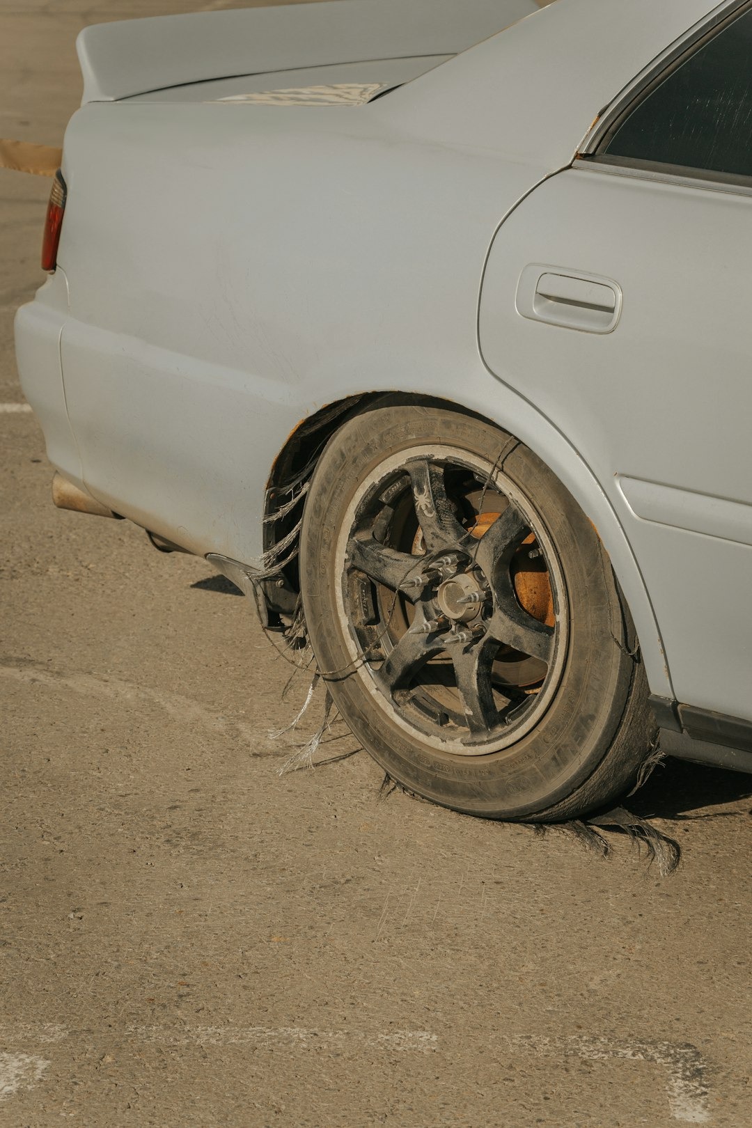 Flat, shredded tire on a light grey sedan.